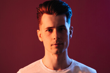 Obraz premium Isolated shot of young serious handsome male with trendy hairdo, wears casual brown t shirt, has serious expression as listens to interlocutor, poses in studio against crimson background