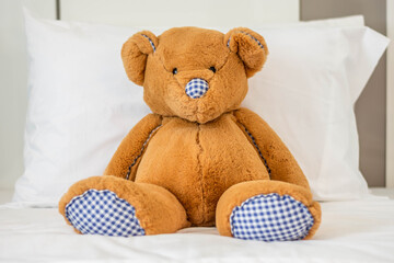 Teddy bear is leaning on the white pillow on the mattress.