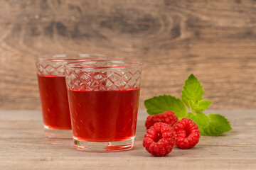 homemade sweet raspberry wine or juice in small glasses with fresh berries on aged wooden table