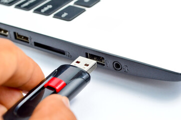 Hand inserting plug in flashdisk into usb port in laptop personal computer, data transfer device concept, close up