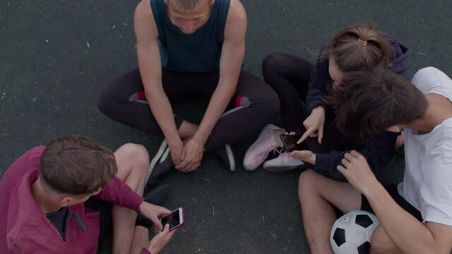 Friends sit on the playground and discuss photos after playing football or playing sports in a sunny day. 4K RAW graded footage