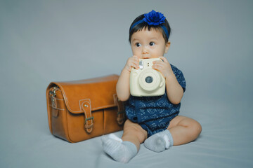 portrait of baby in blue dress and hair bow in concept learning and development in dream with play camera toy and vintage bag