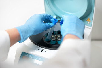 Female's hand in blue glove putting analysis samples into a centrifuge in laboratory.