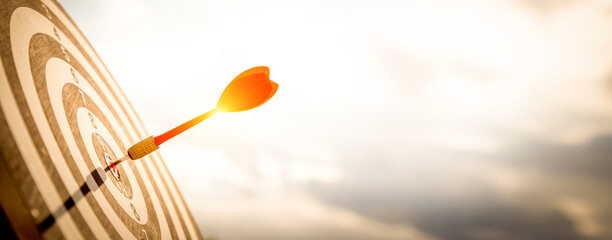 Close up shot red darts arrows in the target  of dartboard center on dark blue sky background. Business target or goal success and winner concept.