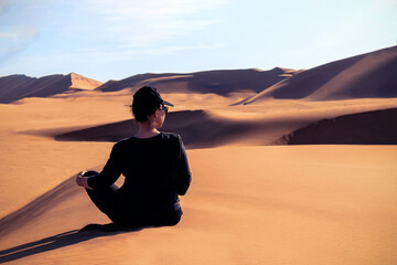 A woman is sitting on the golden sand dune of the Namib desert. Africa