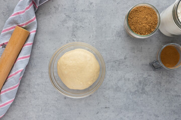 Cinnamon roll dough inside a crystal bowl next to some jars full of cinnamon and vanilla powder.