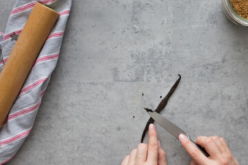 Woman hands extracting Madagascar vanilla seeds with a knife over a grey rustic table.