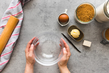 Woman hands holding an empty crystal bowl next to a lot of cinnamon roll ingredients.