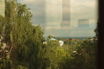 view from the window of the rainbow against the background of trees and the urban landscape after a thunderstorm in summer