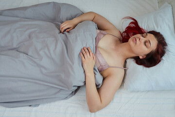 Top view of sleeping woman with red hair lying on her back in bed with closed eyes