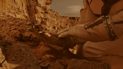 Unrecognizable cosmonaut examining soil on Mars