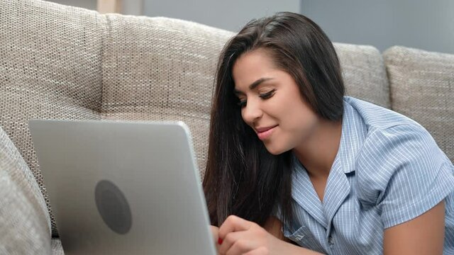Closeup laughing brunette woman chatting online surfing internet lying on couch use laptop relaxing