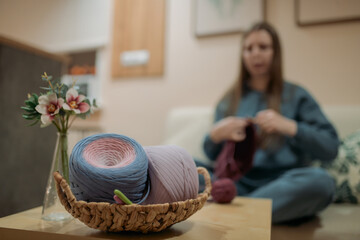 Young woman crochets a basket on the sofa in the living room.