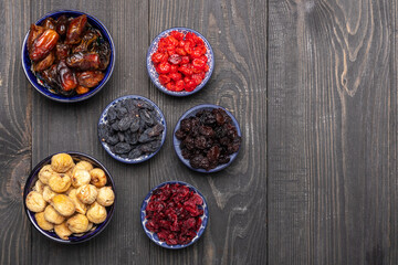 Different dried fruits in bowls on a dark wooden table top view. Dried dates, cherries, raisins, sultanas, cranberries and figs