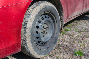 wheel of a dirty red car. The car rim is secured with five nuts.