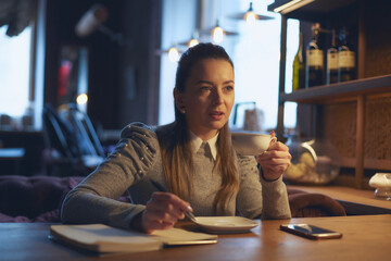 Beautiful woman sitting in a cafe at a table drinking tea and making notes in a notebook