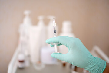 Syringe with cosmetology injection in the hand of the beautician against the background of bottles...