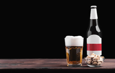 Glass of beer, pistachios and bottle of beer on wooden table with black background