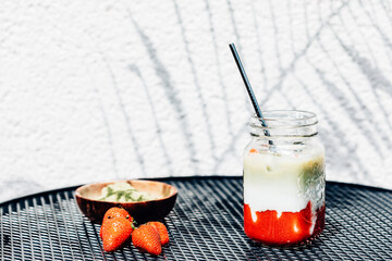 Strawberry matcha latte drink under bright sun and shade from fern