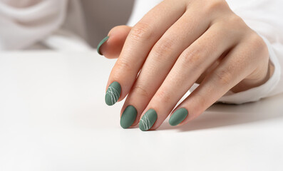 Obraz na płótnie Canvas Hands of a young woman with green olive matte nails on a light gray background. Manicure, pedicure beauty salon concept. Copy space for text or logo. Gel polish and abstract white spider web pattern