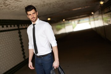 Handsome young businessman walking in underpass, looking away.