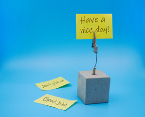 Yellow sticky note with positive attitude message , have a nice day , with stainless steel clamp holder made from cement cube using for reminder and message note , on blue background 