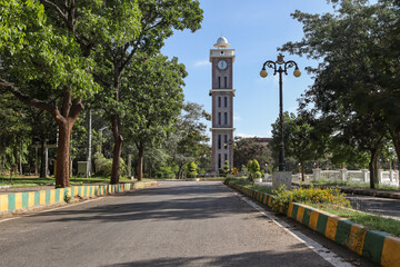 Fototapeta na wymiar A Clock tower in a beautifully landscaped park and the leading street on a mid afternoon in a campus in Karnataka, India.