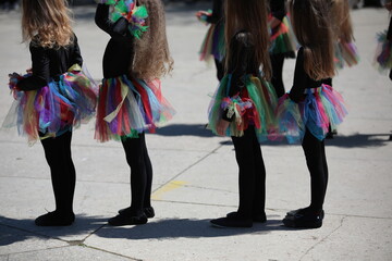 Little girls dancers with long hair in colorful skirts perform at a children's school masquerade in...