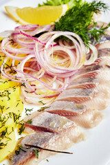 herring with potatoes and onions on a white plate on a light background