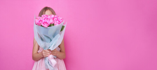 A little girl in pink dress with bouquet of roses, hid behind the flowers.The girl inhales the fragrance of flowers on pink backgraund banner