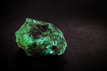 raw emerald on isolated black background, green gem, shiny precious