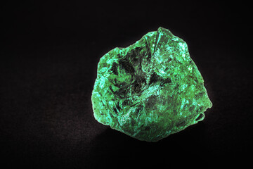 raw emerald on isolated black background, green gem, shiny precious