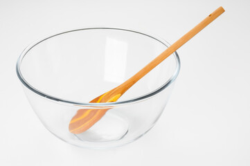 Empty glass food bowl with wooden spoon on white background