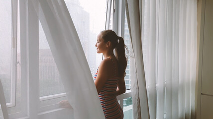 Back view of woman looking through window on the city in the rain.