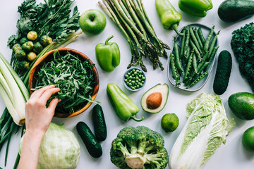 Woman hands taking fresh arugula from wooden bowl on table with fresh vegetables, healthy nutrition concept.