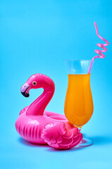 Cocktail tequila sunrise with inflatable pink flamingo pool toy on blue background. Summer concept