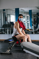 Fototapeta na wymiar Man sitting in the gym with a towel around his neck. Surrounded by machines and weights. Health and wellness concept.