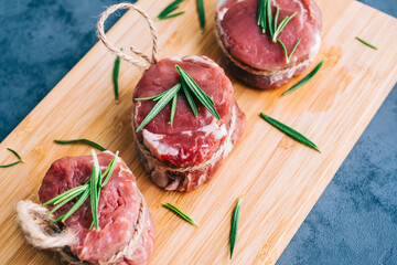 Raw beef filet mignon steak on a wooden board with rosemary and spices.