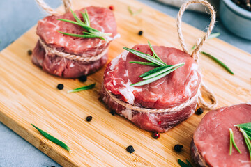 Raw beef filet mignon steak on a wooden board with rosemary and spices.