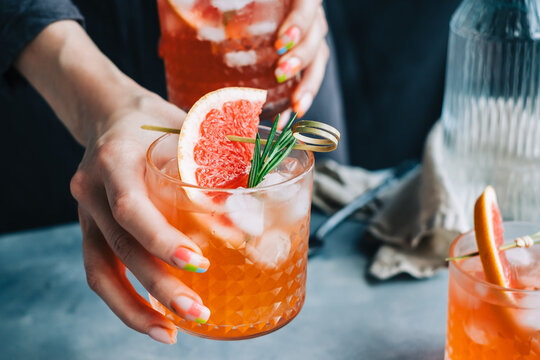 Female bartender hand holding grapefruit cocktail lemonade glasses  with ice and rosemary.
