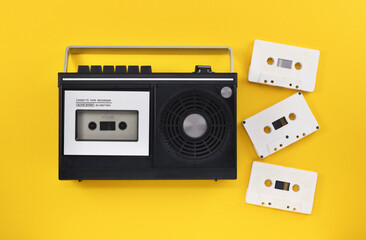 Obraz premium Antiquated retro-style portable stereo radio with cassette recorder and audio cassettes from around the late 70s on a yellow background. Music listening concept. Vintage. 