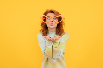 happy redhead woman wear funny party glasses send kiss on yellow background, having fun