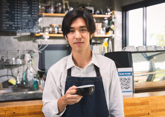 Young asian man servings cup of hot coffee latte standing at counter in coffee cafe shop.