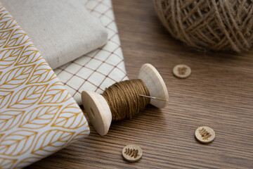 A spool of thread,buttons, scissors, and cotton fabrics on a wooden table