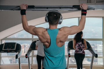 Handsome athlete working out at gym. Pull ups, exercising back. Fitness people.