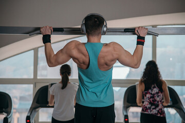 Handsome athlete working out at gym. Pull ups, exercising back. Fitness people.