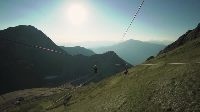 a guy and a girl are flying on a big zip line on a beautiful sunny day in the mountains 