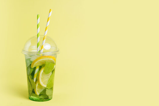 Mojito cocktail in a plastic glass with a tube on a yellow background. ool drink in the summer for takeaway. Place for text.
