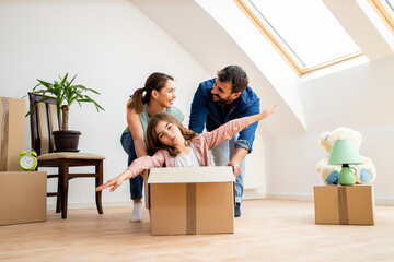 Young caucasian family moving in new apartment and cute little girl sitting in cardboard box.
