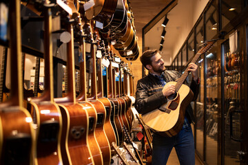 Talented caucasian musician in leather jacket checking the sound of new guitar instrument in music shop.